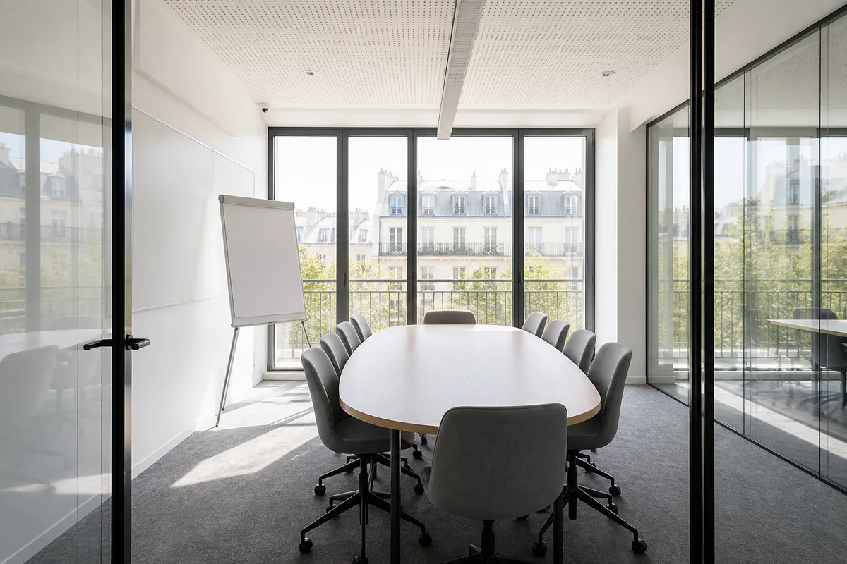 Salle de réunion vitrée avec chaises vides et paperboard vierge dans un immeuble de bureaux parisien