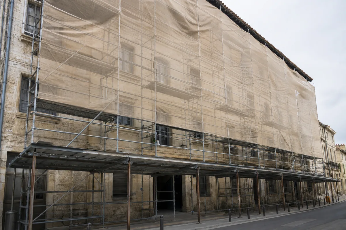 Façade d&rsquo;un immeuble ancien en pierre avec échafaudage métallique et bâche de chantier claire